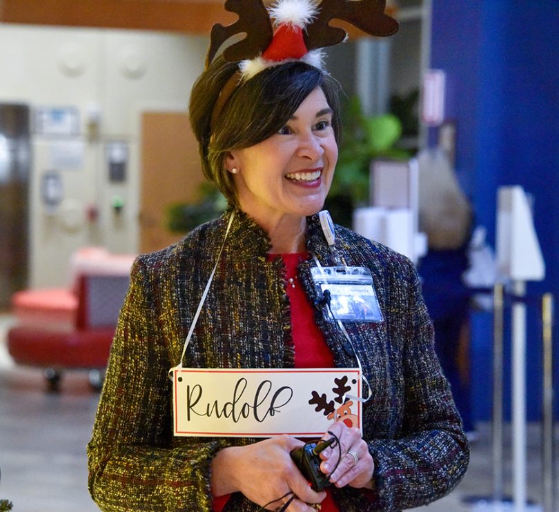 Woman in deer hat and Rudolph sign smiling