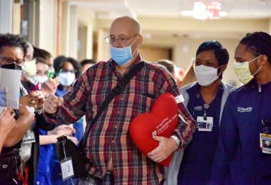 Man holding heart pillow walking down crowded hallway