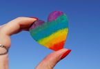 Two fingers holding a rainbow heart