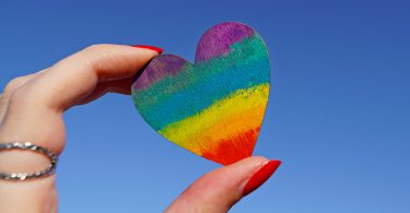 Two fingers holding a rainbow heart