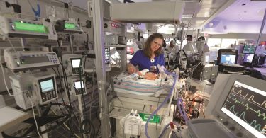 nurse stands over infant connected to medical device