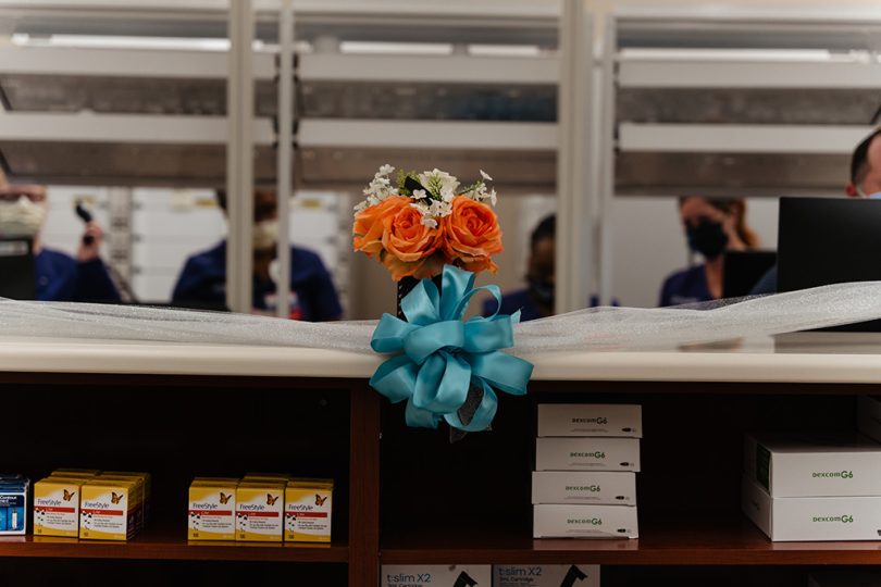Orange bouquet and white ribbon with blue bow on top of shelf with medications