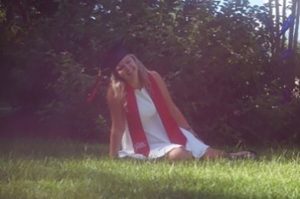 Woman in graduation camp sitting on grass