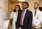 Two men and one woman standing and looking at medical information on white board.