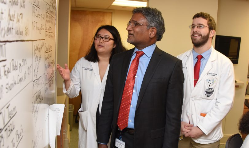 Two men and one woman standing and looking at medical information on white board.
