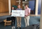 Two teenage boys and a teenage girl hold a large check