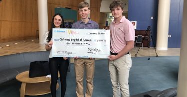 Two teenage boys and a teenage girl hold a large check