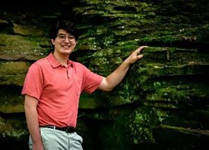 Man in pink shirt standing by wall of rock