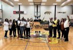 People and jaguar mascot holding banner in school gym