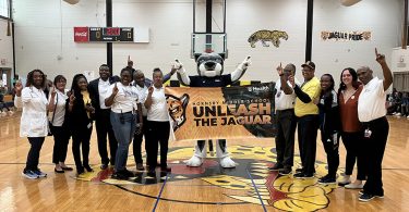 People and jaguar mascot holding banner in school gym