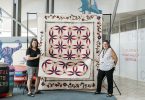 Two women stand in front of a quilt