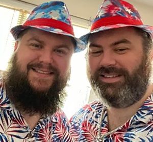 Two bearded men in colorful fedoras dressed alike