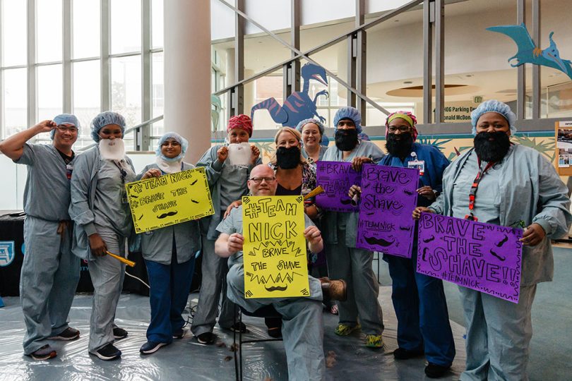 Group of people holding yellow and purple Brave the Shave signs