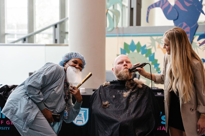 Man getting a beard trim while a nurse in scrubs poses beside him with a fake beard