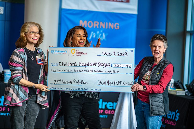 Three women smile and hold big check