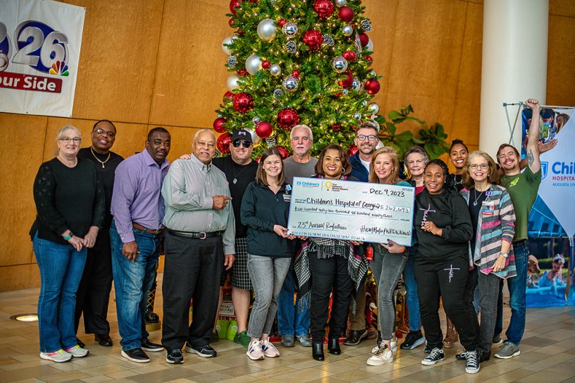 Group of people hold a check in front of Christmas tree