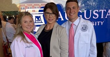 Woman in glasses between two students in medical coats