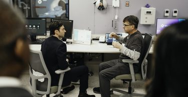 Two men talking in front of a computer and MRI machine