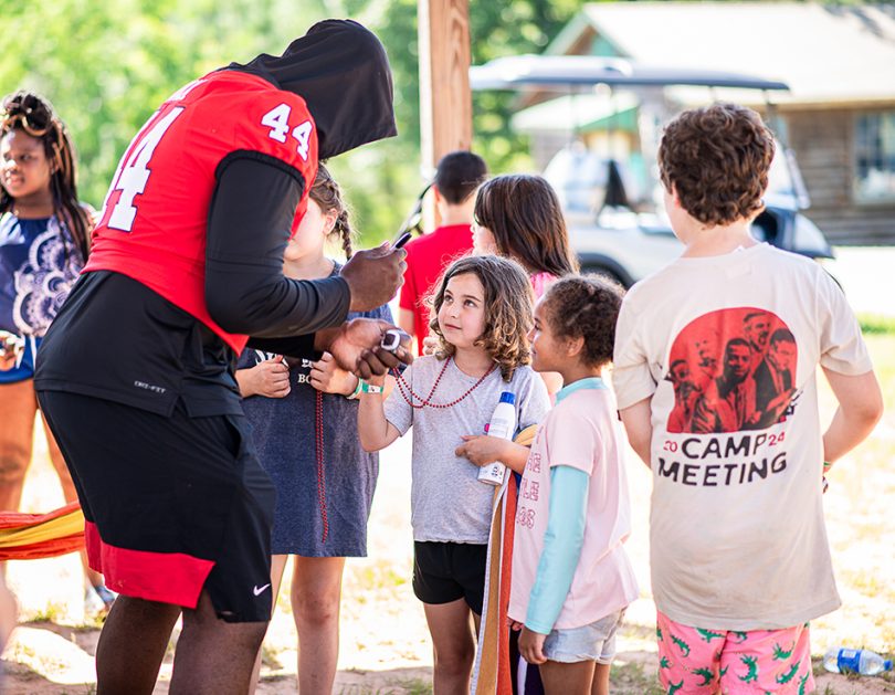 Football player in a red jersey and black hoodie signs an autograph for two little girls