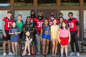 Group of kids and football players pose for a group photo in front of a cabin