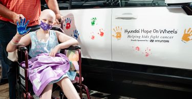Young cancer patient in wheelchair holds up painted hand